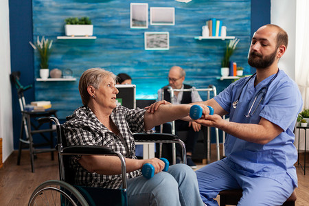 男护士帮助坐在轮椅上的老年退休残疾妇女使用哑铃进行康复
