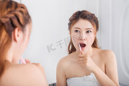 穿着浴巾的女人在浴室里用镜子刷牙