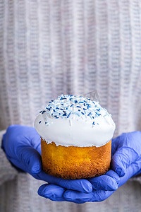 戴着蓝色手套的手拿着带有白色浇头和蓝色洒水的复活节蛋糕。