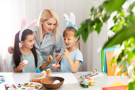 年轻的母亲和她的两个小女儿在家画色彩缤纷的复活节彩蛋