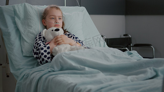 独自忧心忡忡的儿童患者戴着氧气鼻管躺在床上抱着小熊
