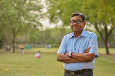 在印度新德里的一个公园里，一位身穿衬衫、双手交叉在户外站立和思考的快乐印度老人的画像