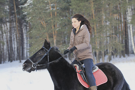 白雪皑皑的森林里骑着黑马的年轻漂亮女人