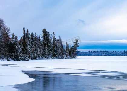 结冰的湖摄影照片_结冰的湖面上多雪的常青松树