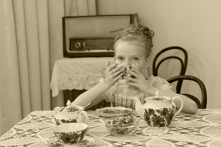 可爱的小女孩在旧桌旁喝茶。