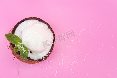 白色冰淇淋球摄影照片_新鲜椰子半块的香草冰淇淋球，装饰着粉红色背景的薄荷叶