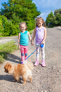 户外遛狗摄影照片_两个小女孩带着小狗在户外遛狗