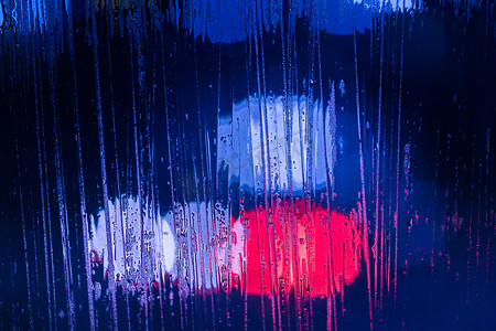 红色和蓝色警灯的抽象背景在夜间通过湿玻璃特写，有选择地聚焦