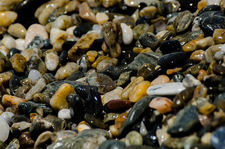 蓝色海浪装饰摄影照片_海浪冲刷的卵石滩，形成海岸的各种小石头