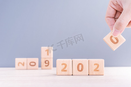摘要 2020 年和 2019 年新年倒计时设计理念 — 女性在木桌和蓝色背景上拿着木块立方体，特写，复制空间。