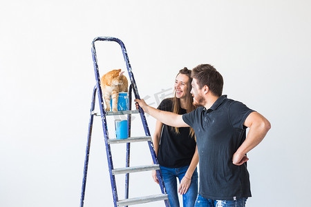 粉刷滚筒摄影照片_修理、翻新、宠物和爱情情侣概念 — 年轻的家庭有猫一起修理和粉刷墙壁并大笑