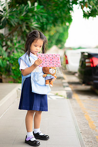 拿着礼物盒的泰国校服的亚裔小女孩并且做