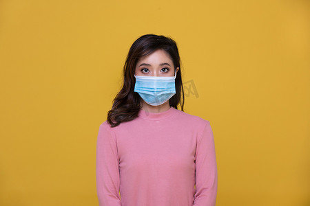 黄色背景下戴着面罩或防护面罩以抵御冠状病毒危机或 COVID-19 爆发的亚洲美丽快乐年轻女性肖像