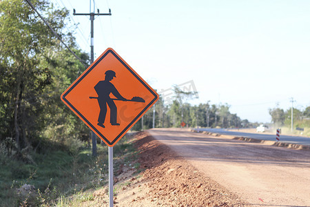 橙色标志显示了一个符号，上面有一个人拿着铲子的图像，在安装在施工道路一侧的标志上。