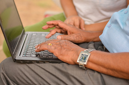 印度新德里一座公园红色长椅上，一位年轻印度女孩的手在笔记本电脑上帮助/教导一位印度老妇人的手部特写