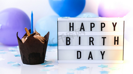 带有文字“生日快乐”的灯箱和抽象的离焦模糊节日背景上的巧克力蛋糕蜡烛。