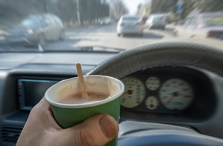 司机手里拿着一杯可可、巧克力和热饮，他正在驾驶一辆沿着城市街道行驶的汽车