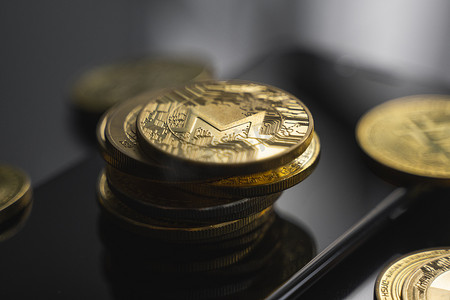 智能手机上的一叠金色 Monero 比特币硬币，桌子上有很多比特币硬币。