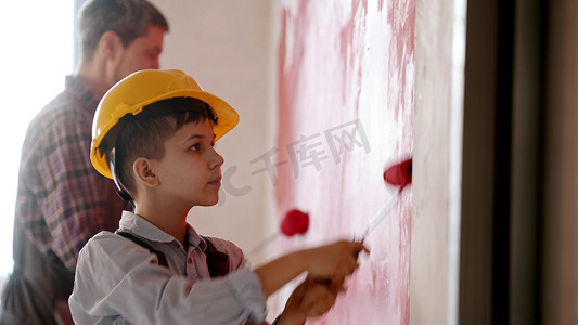 一个小男孩和他微笑的父亲用红色粉刷墙壁