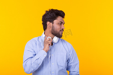 留着胡子的帅气放松的印度男人正在黄色背景的耳机里听着最喜欢的音乐，有复制空间。