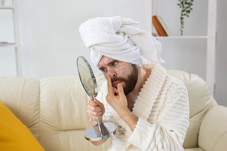 皮肤斑点摄影照片_留着胡子的男人检查他脸上的皮肤。