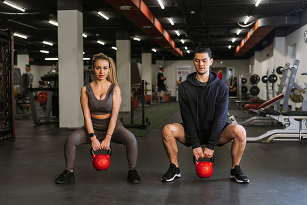 穿着运动服的健身夫妇在健身房里蹲着举重和做深蹲。