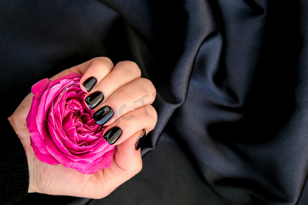 黑色指甲修指甲在黑色丝绸织物上举行粉红色玫瑰花。