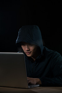 穿着深色连帽衫的黑客坐在笔记本前。