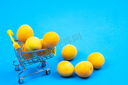 蓝色背景上装有杏子的购物篮。购物车