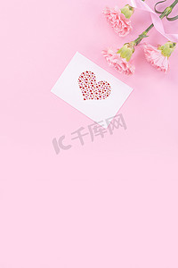 粉红色背景图摄影照片_美丽、清新优雅的康乃馨花束与白色问候感谢礼品卡隔离在明亮的粉红色背景、顶视图、平躺概念。