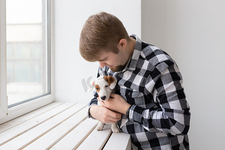 人、宠物和动物的概念 — 年轻人在白色背景的窗户附近拥抱小狗