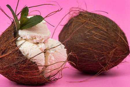 粉红色背景中用薄荷叶装饰的空椰子中的香草冰淇淋球