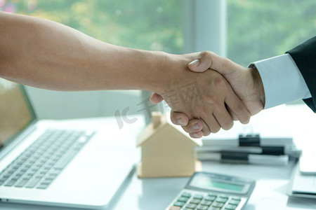 房地产经纪人在签订购房合同后坐在办公桌前与客户握手。