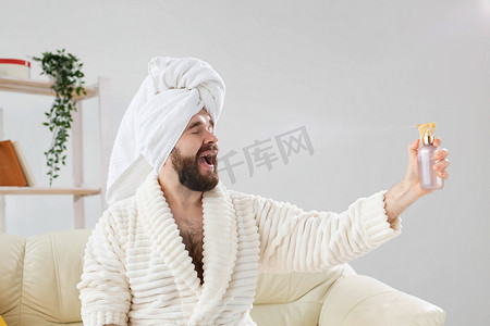 留着胡须的男性头上戴着浴巾，在脸上喷水处理。