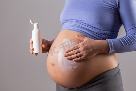 幼儿拉肚子摄影照片_孕妇在她的肚子上涂抹润肤霜