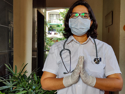 一位年轻医疗保健女工的画像，双手交叉/折叠成合十礼，肩上戴着外科口罩和听诊器，以保护自己免受冠状病毒（COVID-19）流行病的侵害