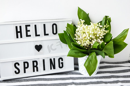 带有文本 HELLO SPRING 的灯箱和白色桶中的铃兰花束，春天
