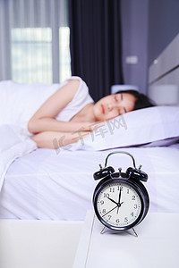 尾迹摄影照片_桌上的闹钟和睡在卧室床上的女人