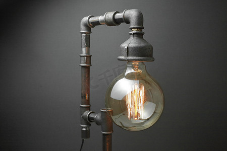 复古灯由金属水管制成，灰色背景上有一盏爱迪生灯。