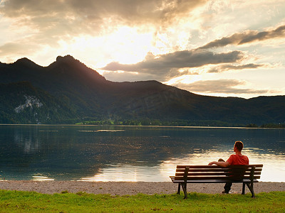一个人坐在湛蓝的山湖边的长凳上。