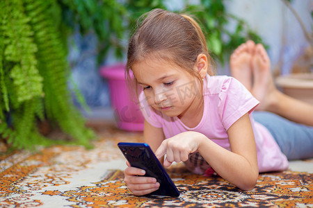 一个女孩躺在地板上玩智能手机。