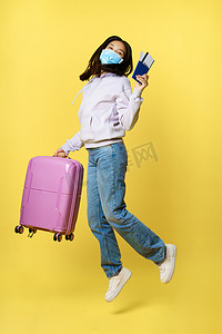 旅游黄色背景摄影照片_全长拍摄快乐的亚洲女人带着手提箱和门票在旅游中跳跃，拿着护照，去度假，站在黄色背景上