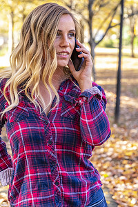 可爱聊天摄影照片_秋天的一天，一个可爱的金发女郎在公园里用她的移动设备聊天