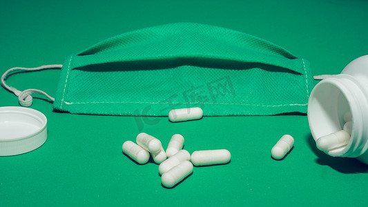 医疗面罩，散落在胶囊中的药片，维生素，治疗，健康的生活方式，绿色背景，特写。