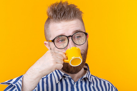 可爱自信的年轻人站在黄色背景下，喝着黄色小杯子里的咖啡。