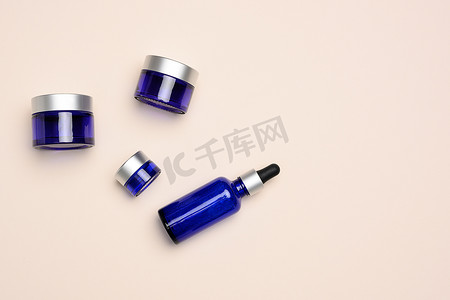 米色背景上带有吸管和罐子的蓝色化妆品玻璃瓶。