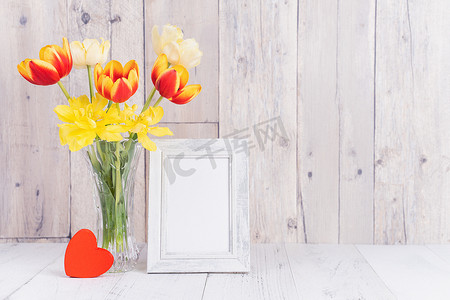 装饰空白背景墙摄影照片_玻璃花瓶中的郁金香花，在家里的木桌背景墙上装饰着相框，特写，母亲节的设计理念。