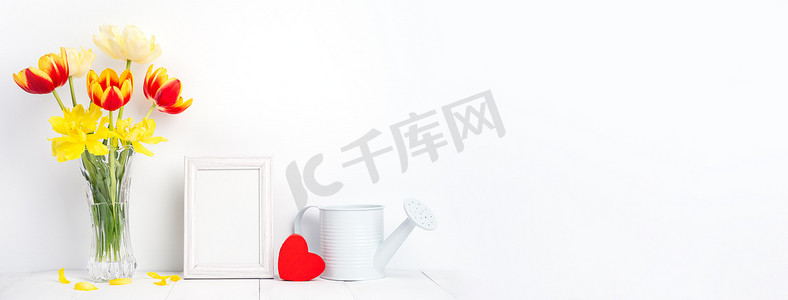 家里墙壁摄影照片_玻璃花瓶中的郁金香花，相框放在白色木桌背景上，与家里干净的墙壁相映成趣，特写，母亲节装饰概念