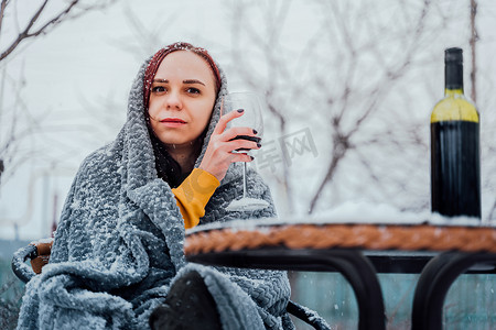 下雪院子里摄影照片_年轻女子坐在院子里，在下雪的天气里喝红酒。