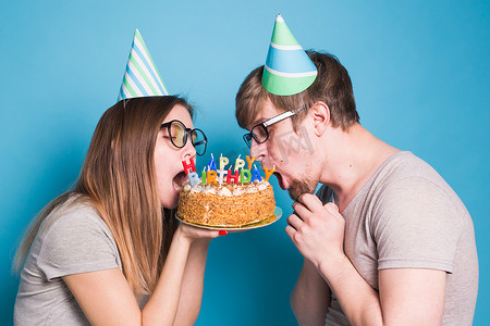 戴着纸帽子的奇怪的年轻夫妇女孩和男孩想咬掉一块祝贺蛋糕。